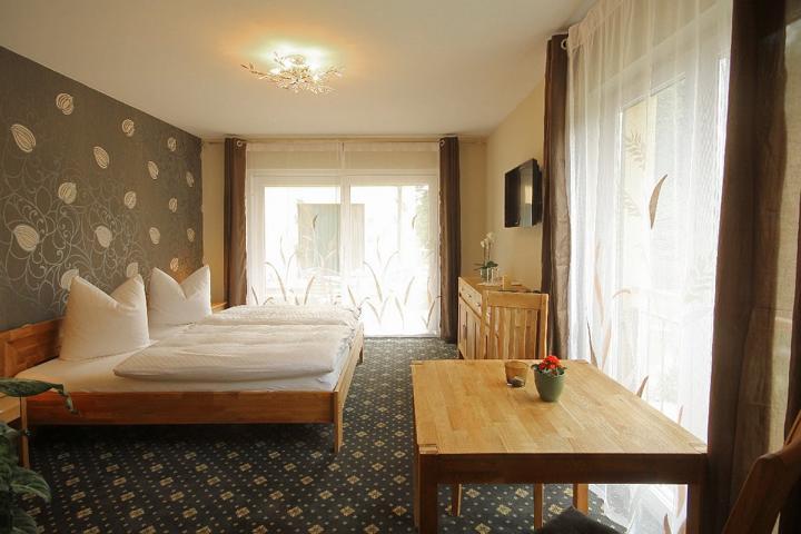 Doppelzimmer im Haus 1 - Blick auf das Doppelbett - Mustertapete auf der Seite vom Kopfteil des Bettes - Blick über den Tisch über die Kommode zum Fenster