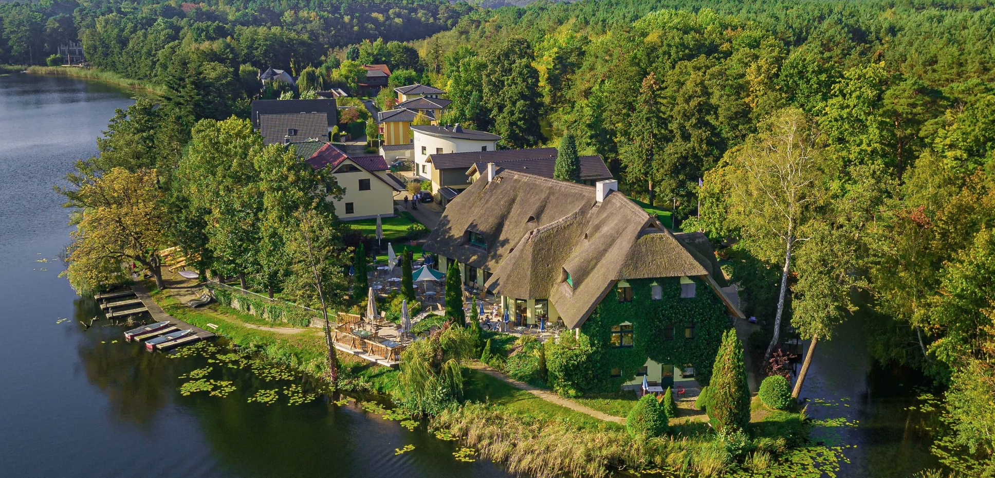 Drohnenbild von der Seite des kleinen Glubigsee über die Restaurantterrasse auf das reetgedeckte Fischhaus