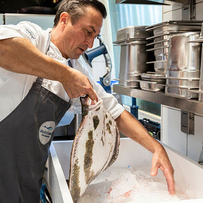 Kuechenchef entnimmt einen Fisch aus der Anlieferungsbox gefüllt mit crashed Eis